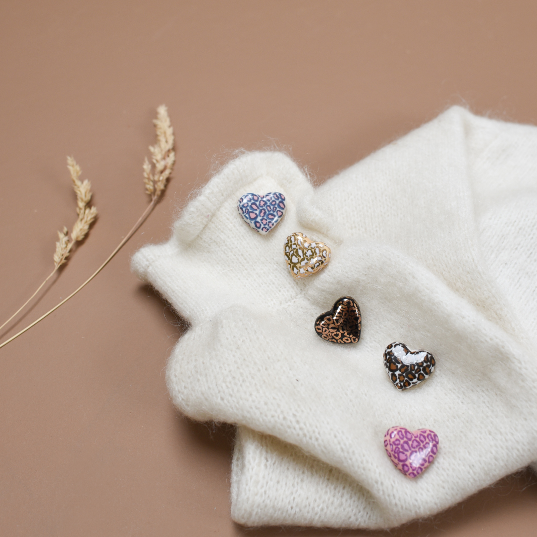 Photo de plusieurs pins ou broches en forme de coeur. Le motif Léopard y est inscrit en plusieurs couleurs, de la marque Baubels